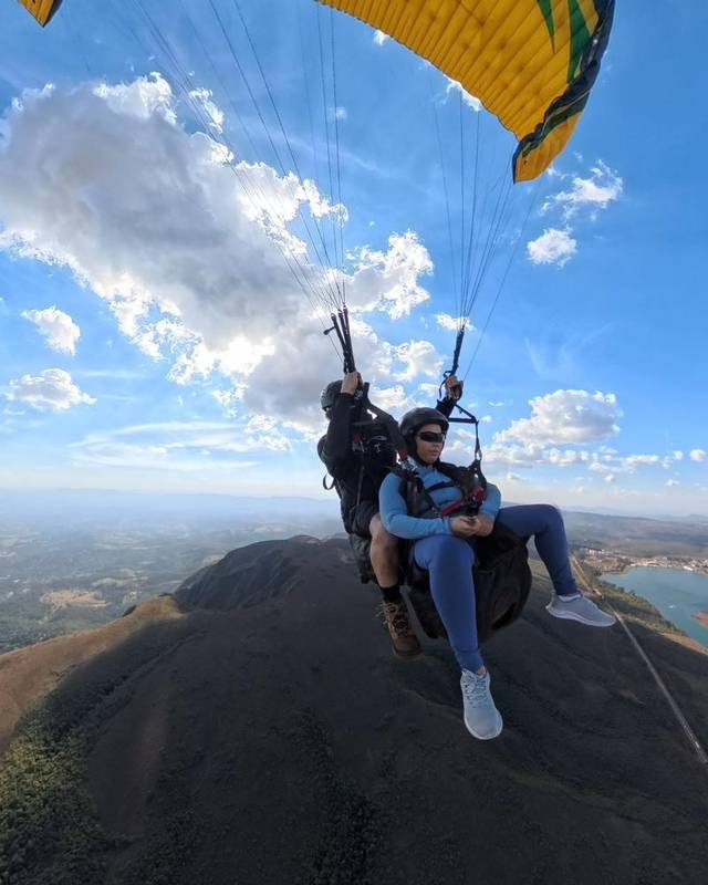 Piloto e passageira em voo duplo sobre a serra, com uma represa ao fundo