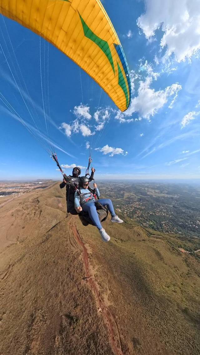 Voo duplo de parapente sobre a Serra da Moeda, com céu azul e a vela amarela aberta